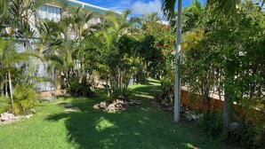 A lush garden with palm trees and a pathway leading to a building with a white facade. - Studio tout confort dans son écrin de verdure au pieds de la Marina (Saint-François)