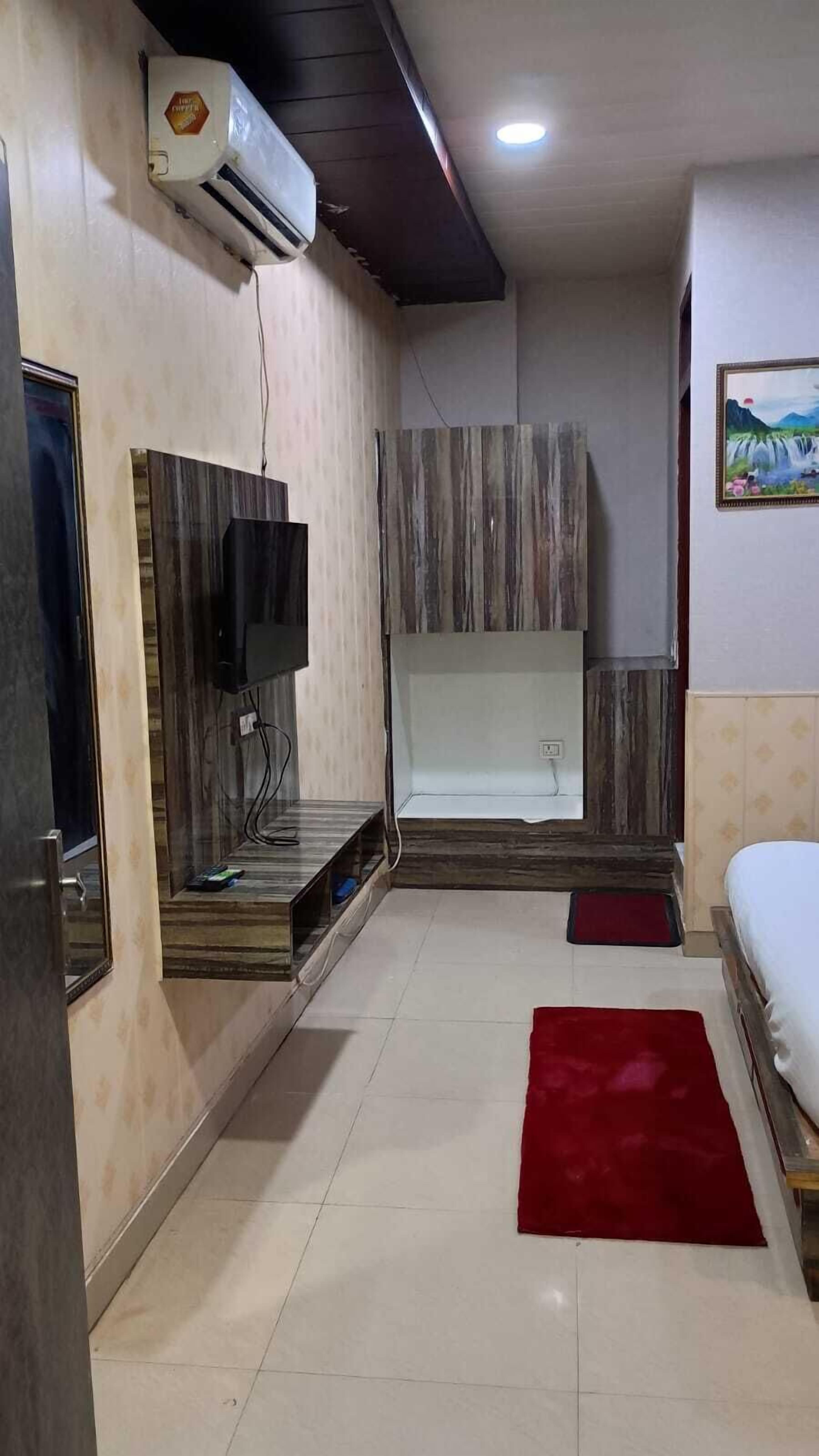 A bedroom with a bed, a red rug, a TV, and a wall-mounted air conditioner.