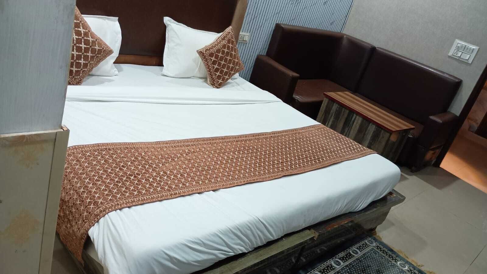 A neatly made bed with a patterned bedspread and pillows, a wooden headboard, and a small seating area with a bench and a chair.