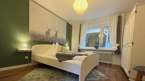 A bedroom with a bed, a window with curtains, a radiator, and a wall-mounted artwork of deer. - 2 bedroom bungalow with kitchen, dining and living room with garden & terrace  (Bispingen)
