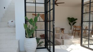 A modern interior with a staircase, a large potted plant, a glass door, and a seating area with a sofa and a chair. - Villa Valeria (Canggu)