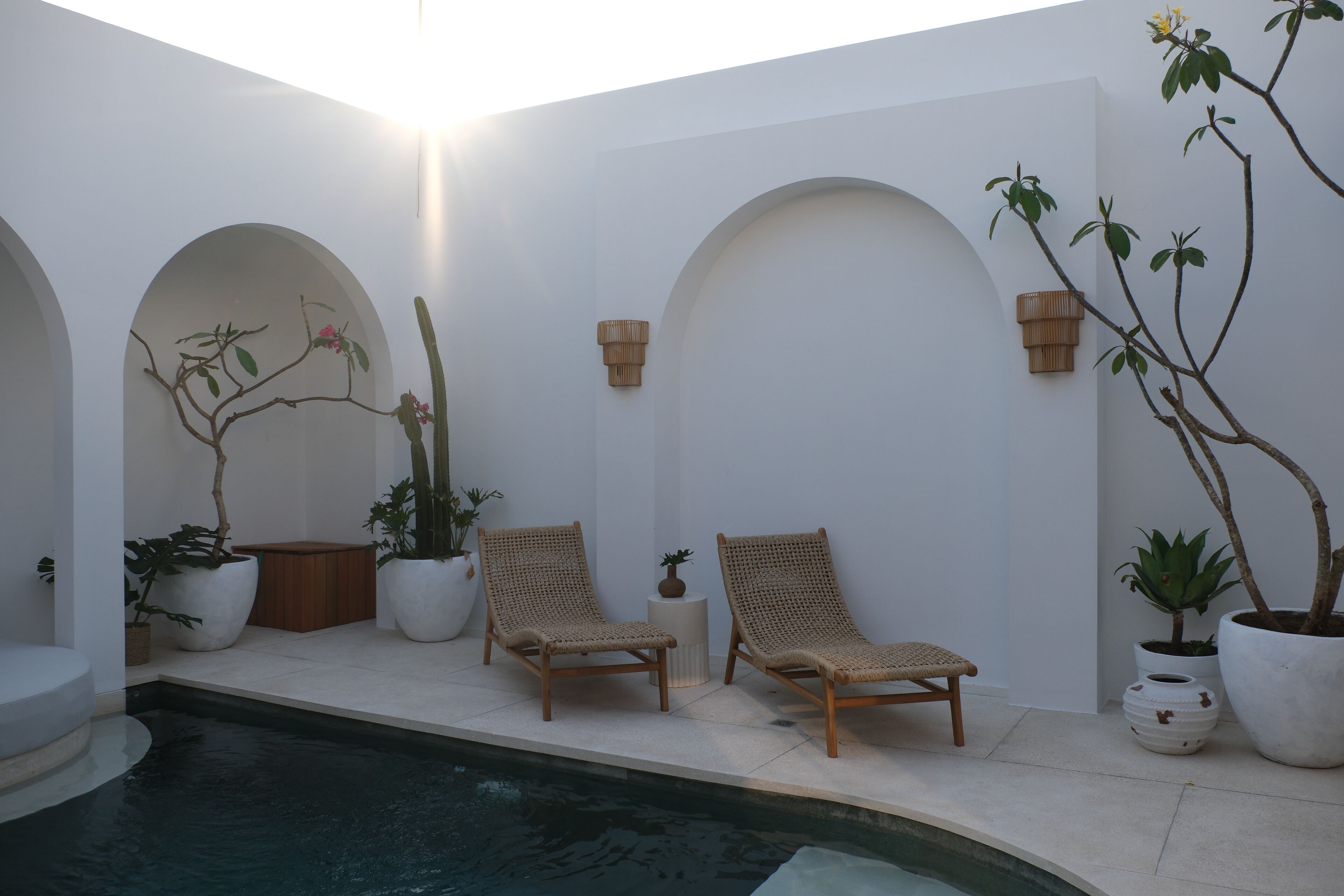 Un área junto a la piscina con dos sillones de mimbre, plantas en macetas y una mesita.