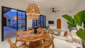A modern dining area with a round wooden table, woven placemats, and wicker chairs. - Villa Valeria (Canggu)