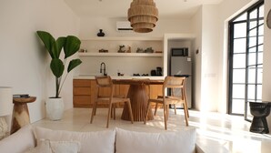 A modern kitchen with wooden cabinets, a dining table, and chairs. There is a large potted plant and a hanging light fixture. - Villa Valeria (Canggu)