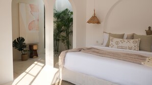 A bedroom with a bed, a hanging light, and a view of a plant through an archway. - Villa Valeria (Canggu)