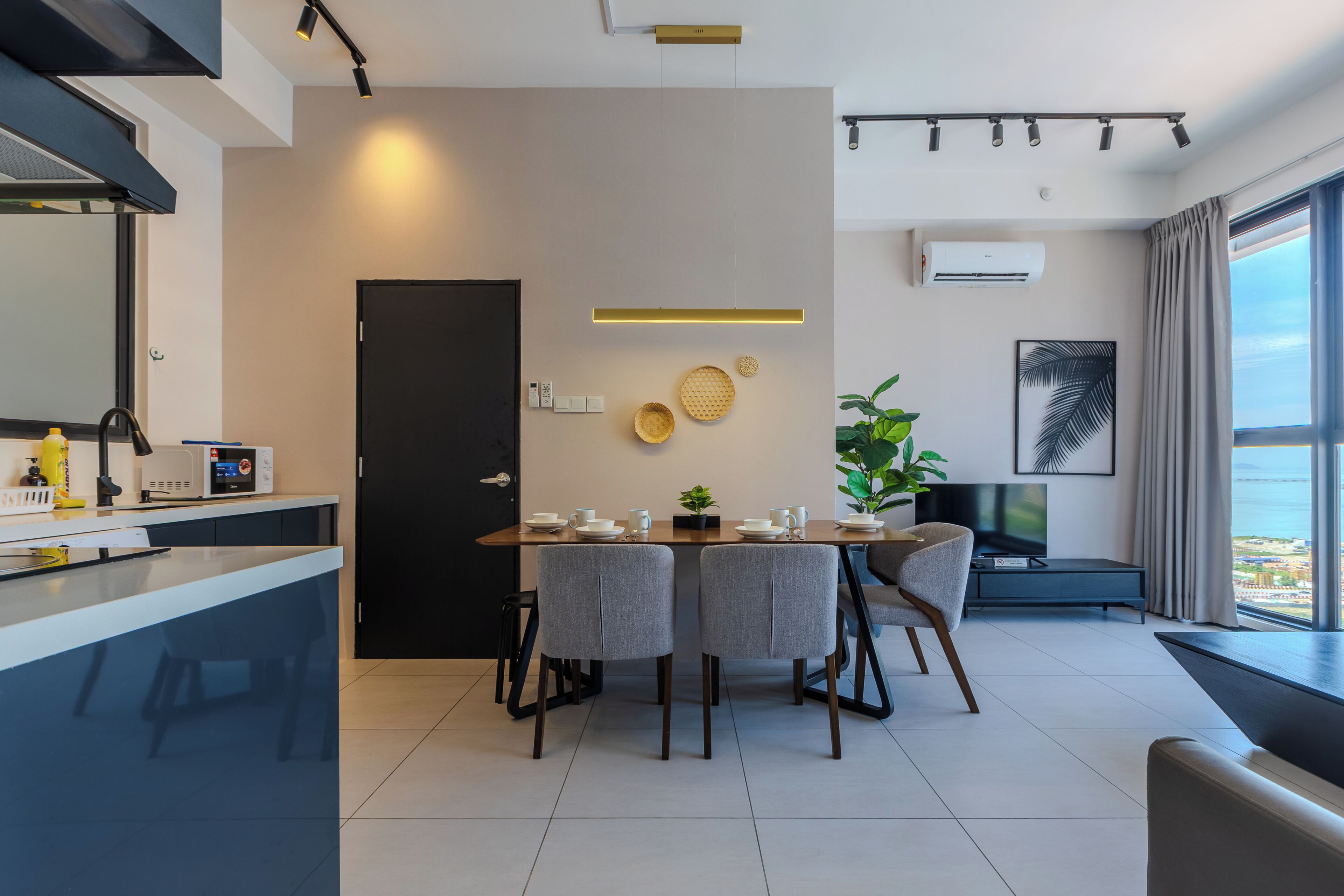 A modern kitchen with a dining area, a black door, and a large window with a view.