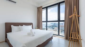 Ein Hotelzimmer mit einem großen Bett, einem Holzmaleimer und Blick auf die Stadt durch große Fenster.