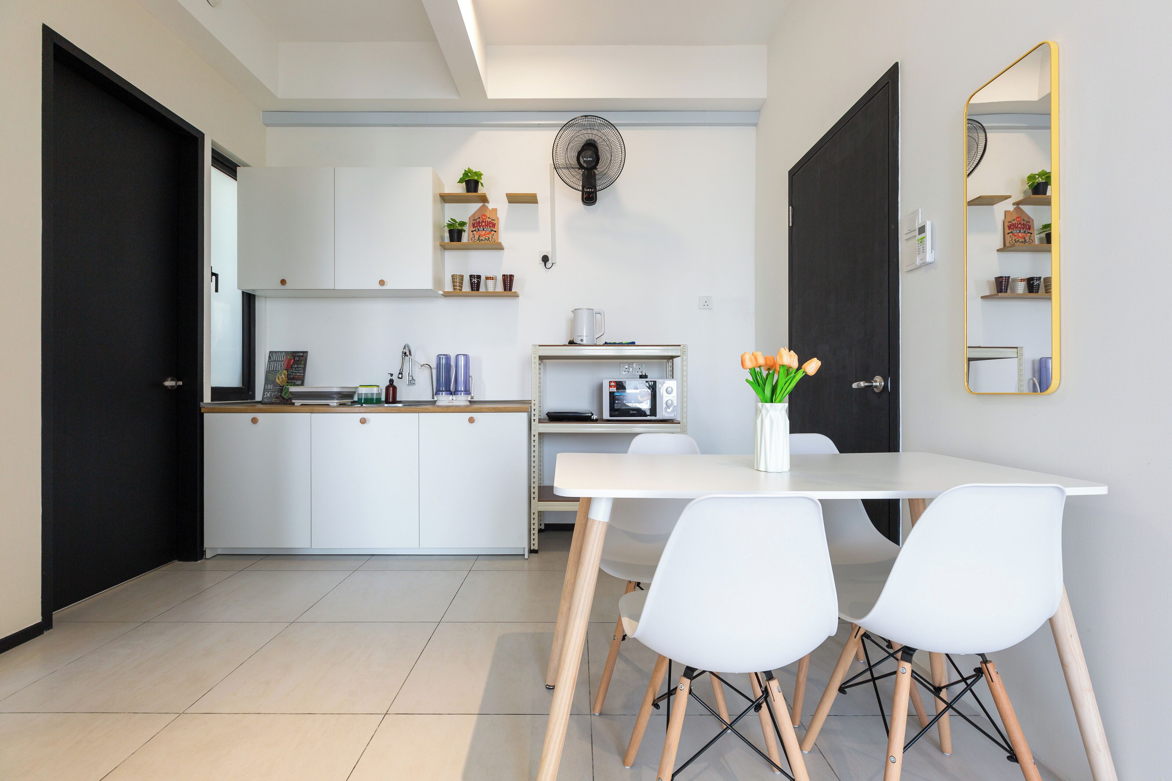 A modern kitchen with white cabinets, a microwave, and a coffee maker. There is a dining table with white chairs and a vase with flowers.