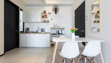 A modern kitchen with white cabinets, a microwave, and a coffee maker. There is a dining table with white chairs and a vase with flowers.