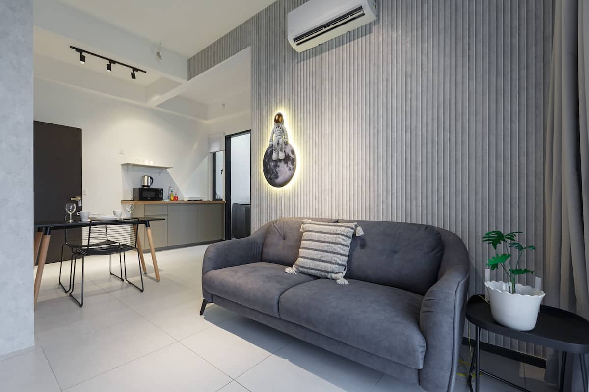 A modern living room with a grey sofa, a dining area with a table and chairs, and a kitchen in the background.