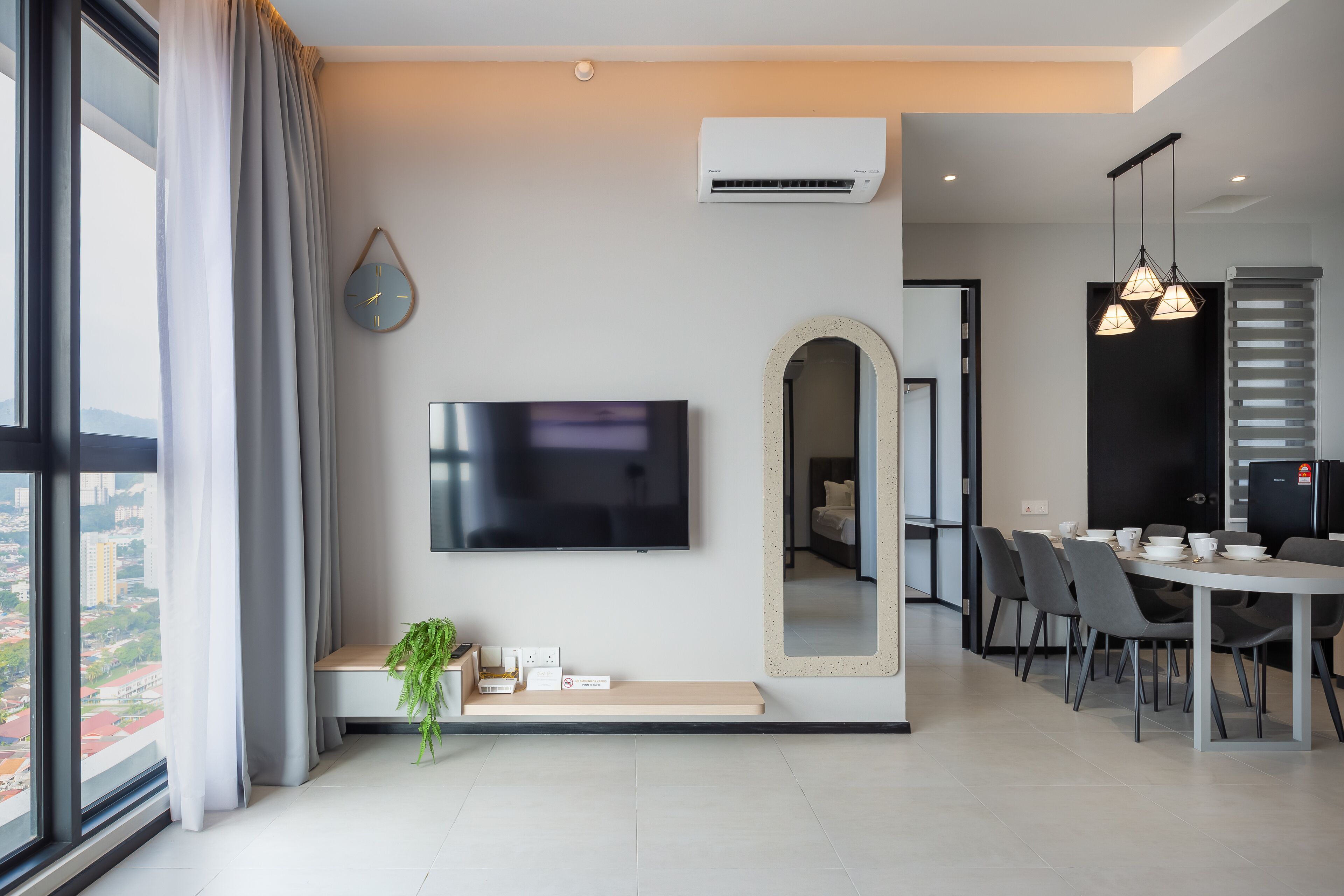 A modern living room with a flat-screen TV, a large mirror, and a dining area with chairs and a table.