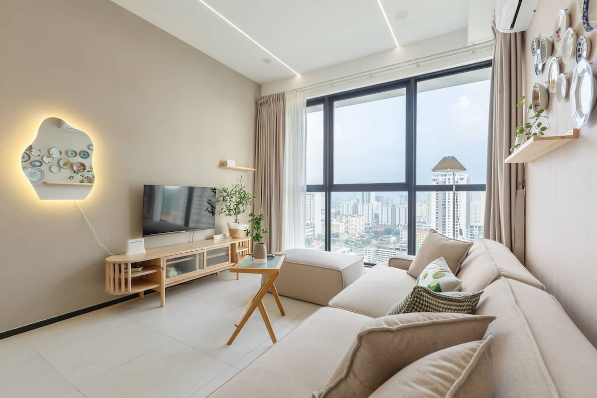 A modern living room with a large window, a flat-screen TV, a sofa, and a small table with decorative items.