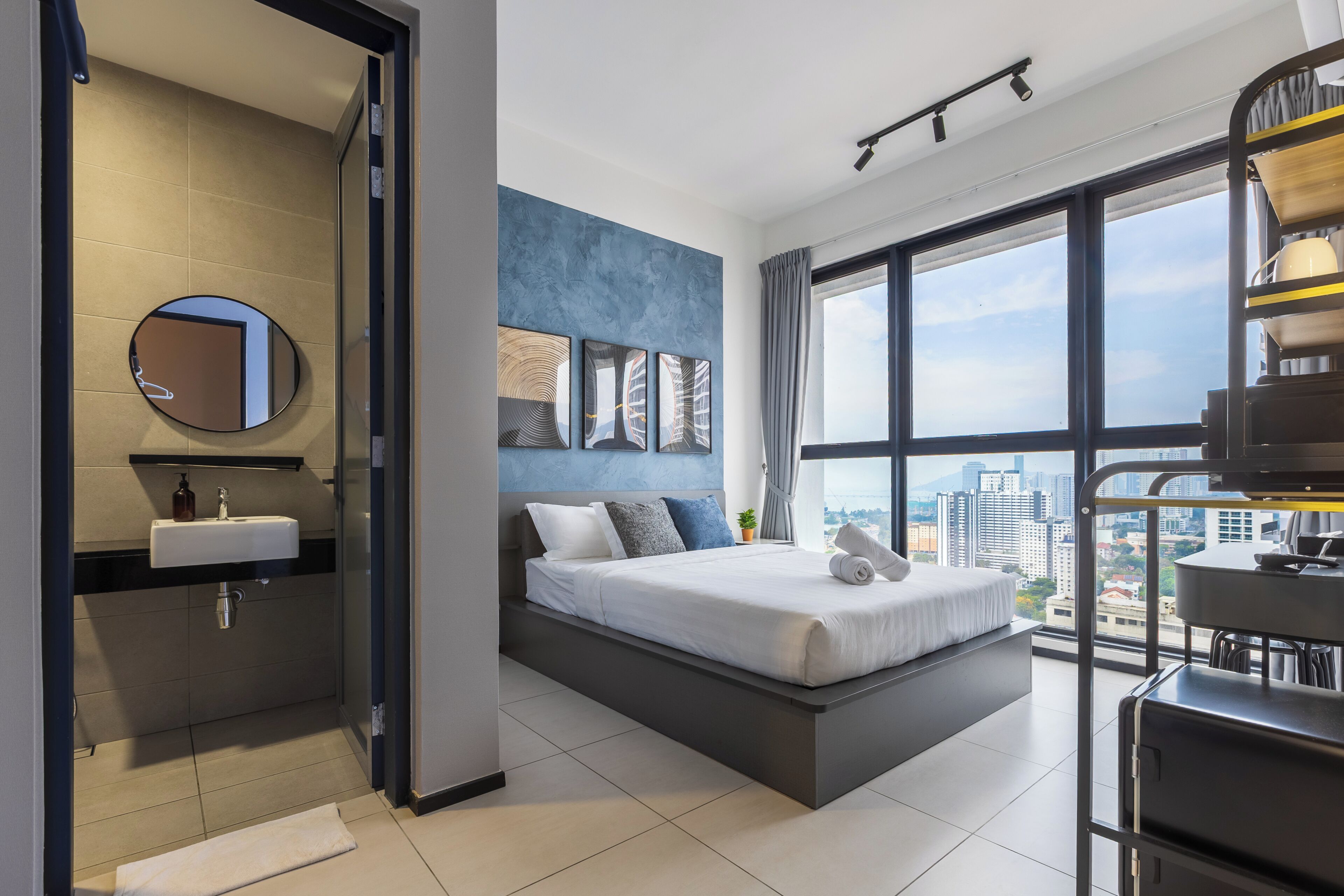A modern hotel room with a large bed, a bathroom with a sink, and a city view.