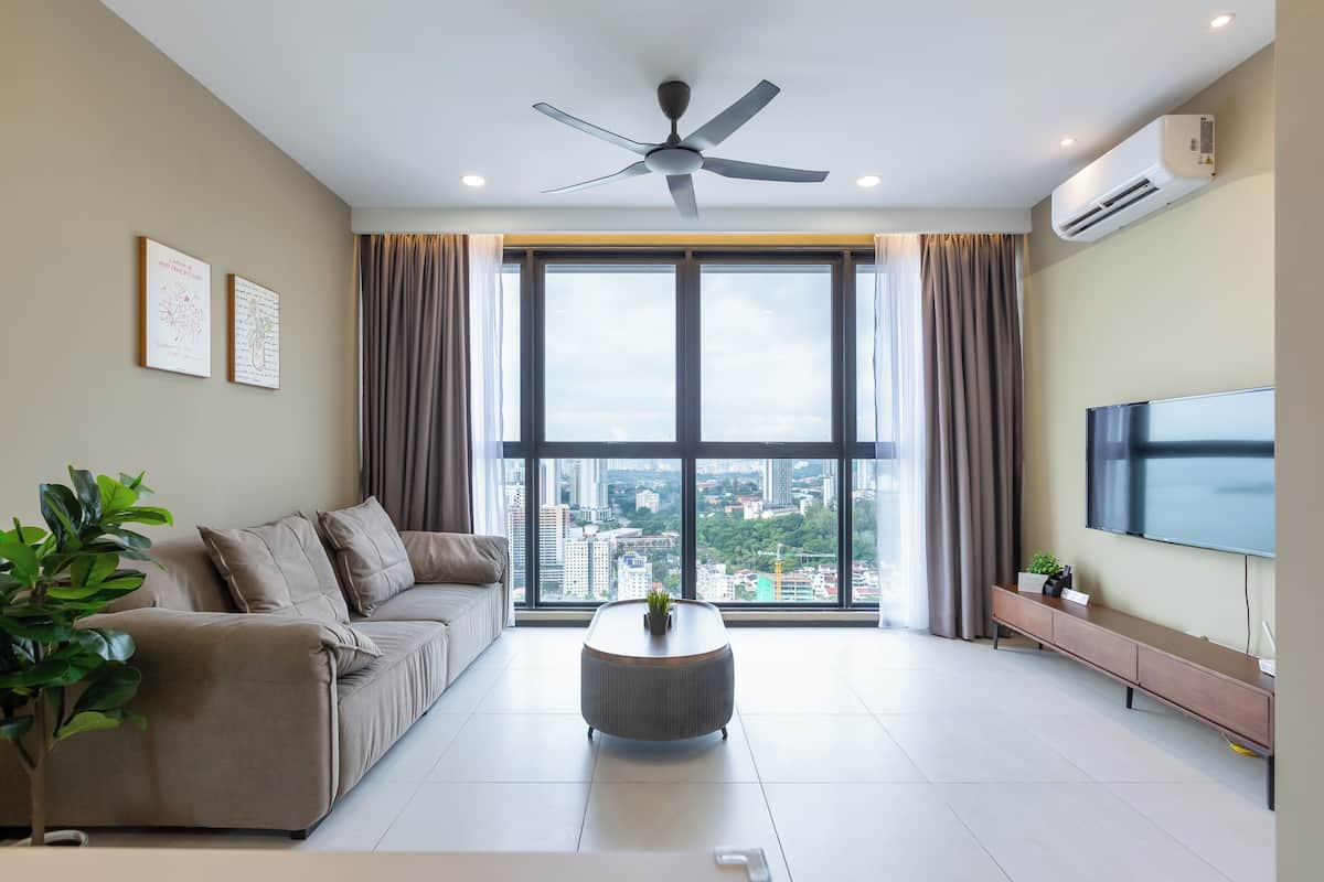 A modern living room with a sofa, a coffee table, a ceiling fan, a TV, and large windows with a city view.