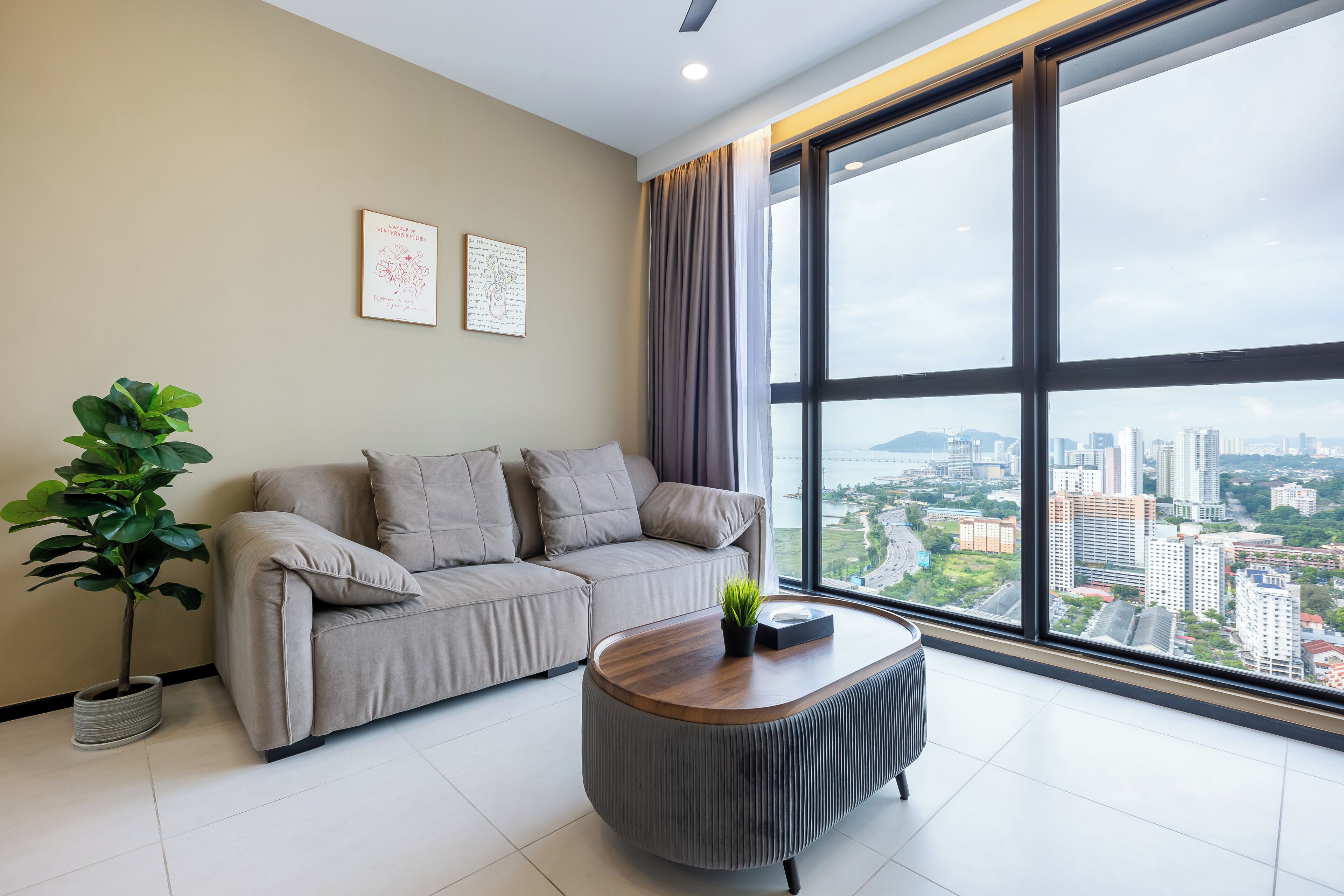 A modern living room with a sofa, a coffee table, and a large window offering a city view.