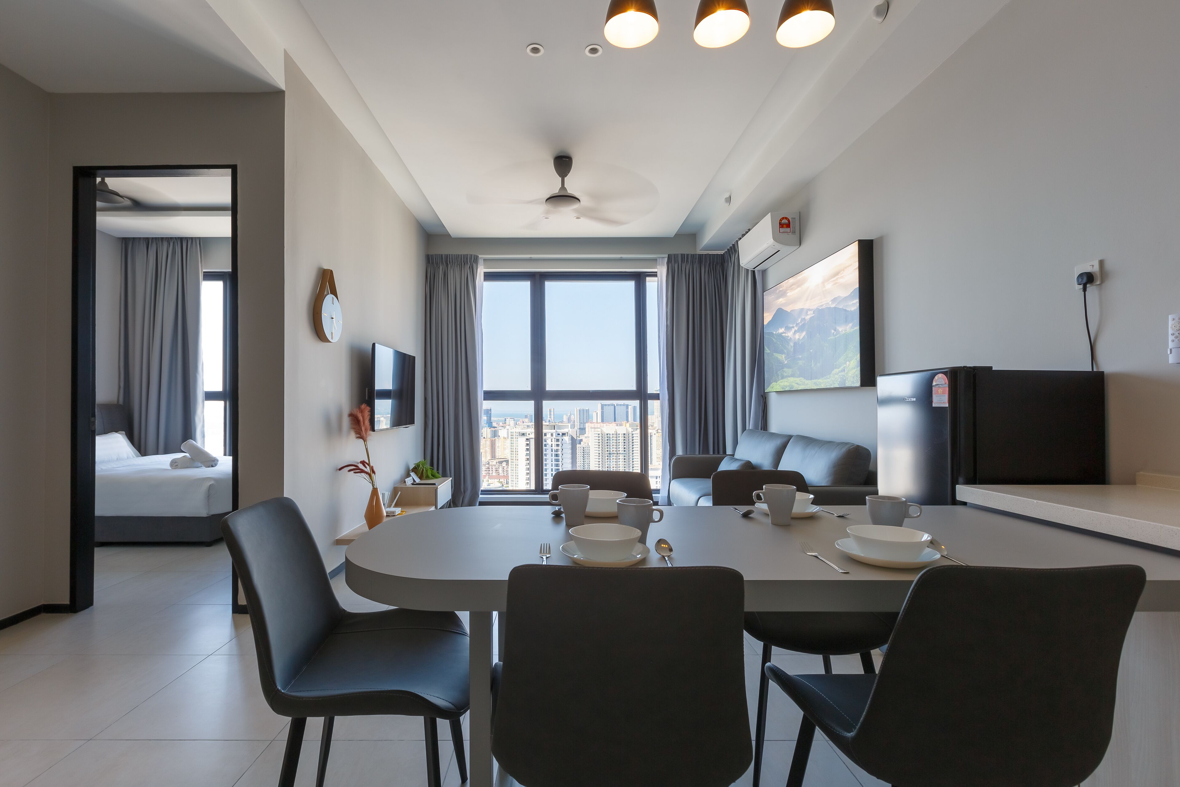 A modern hotel room with a dining area, a bed, a TV, and a view of the city.