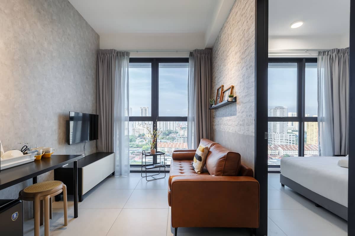 A modern hotel room with a sofa, a bed, a TV, and a desk with a chair.