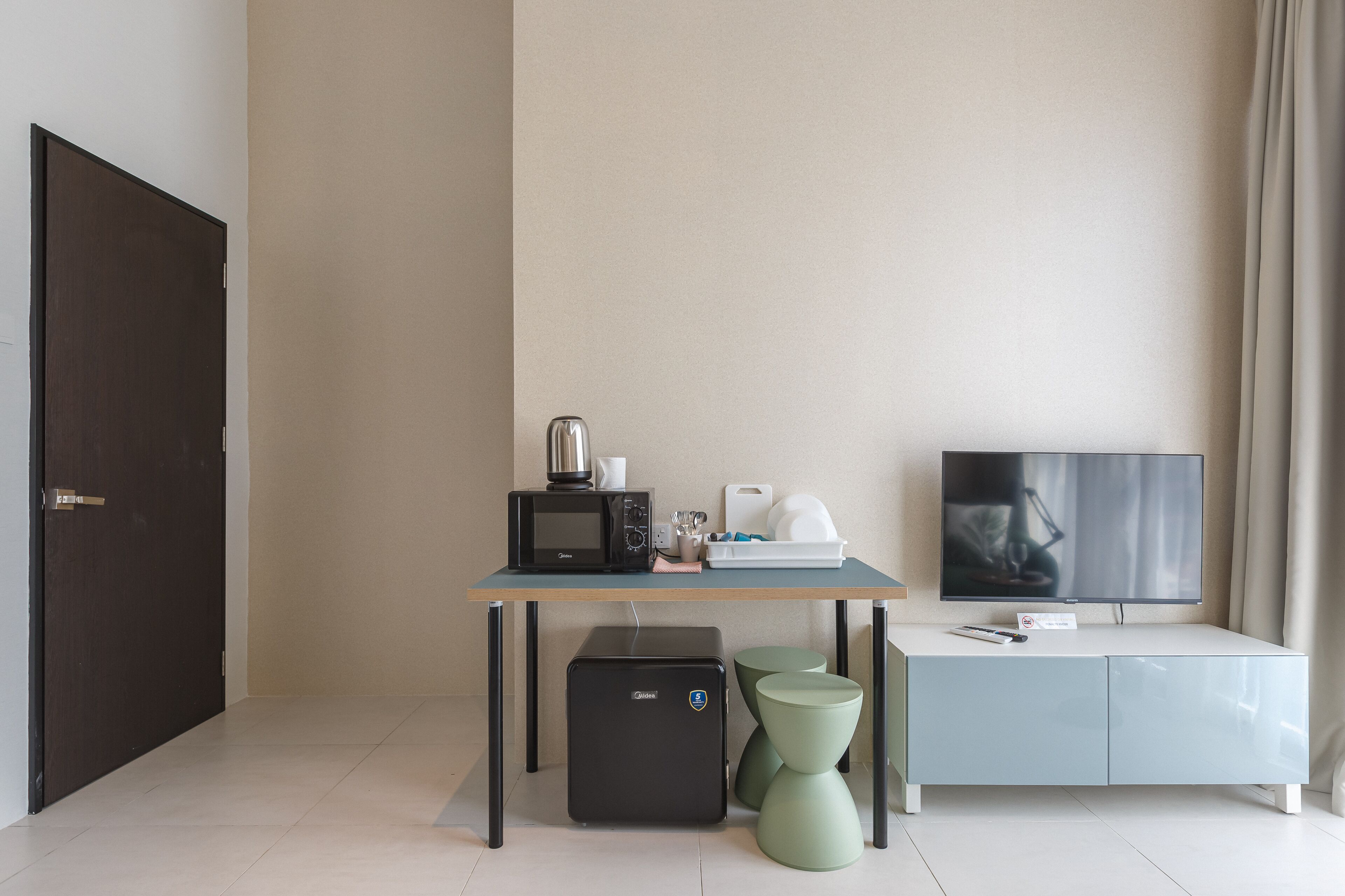 Una habitación moderna con escritorio, televisión, microondas y refrigerador pequeño.