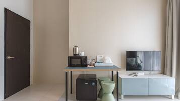 Una habitación moderna con escritorio, televisión, microondas y refrigerador pequeño.