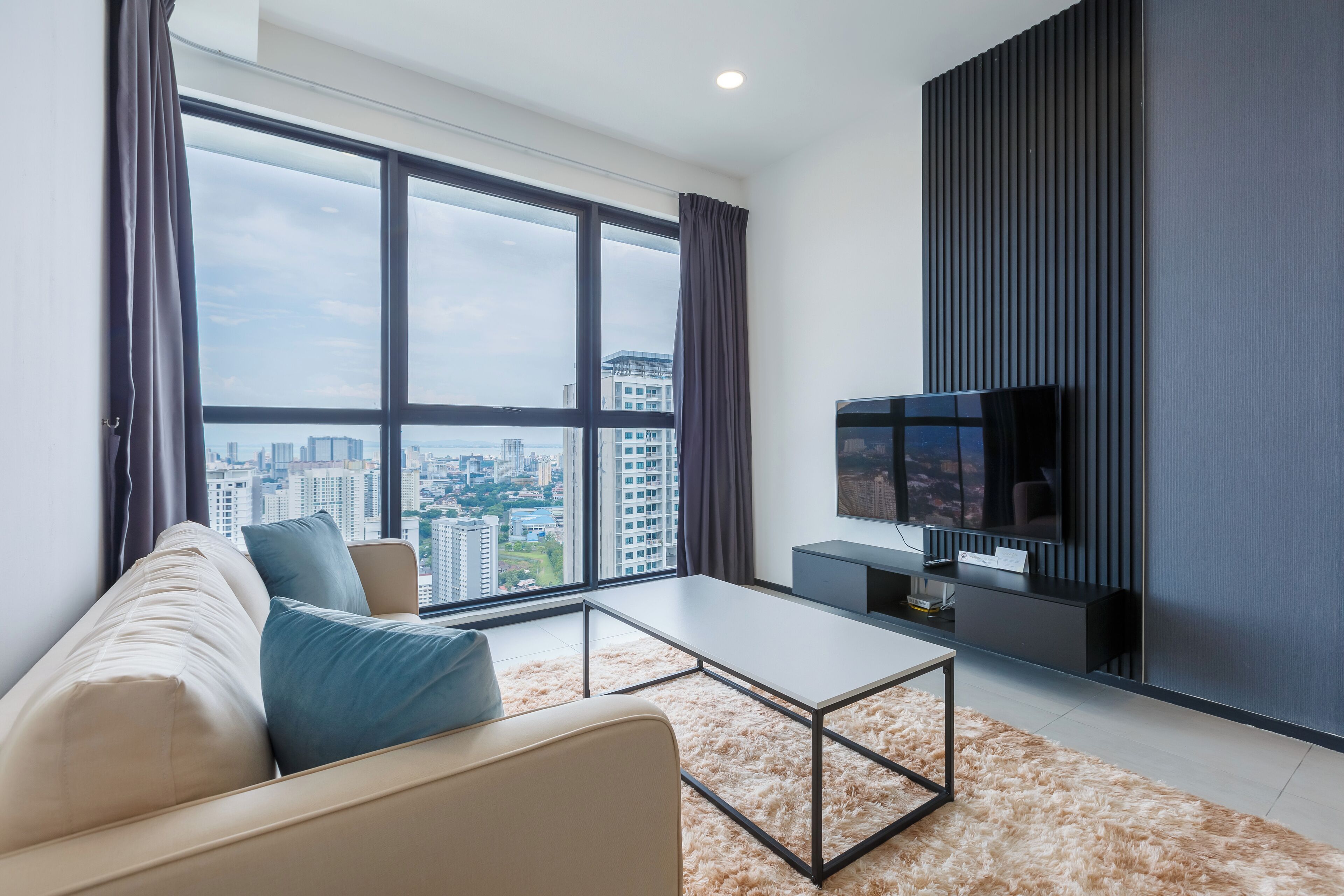 A modern living room with a large window, a sofa, a coffee table, and a TV.