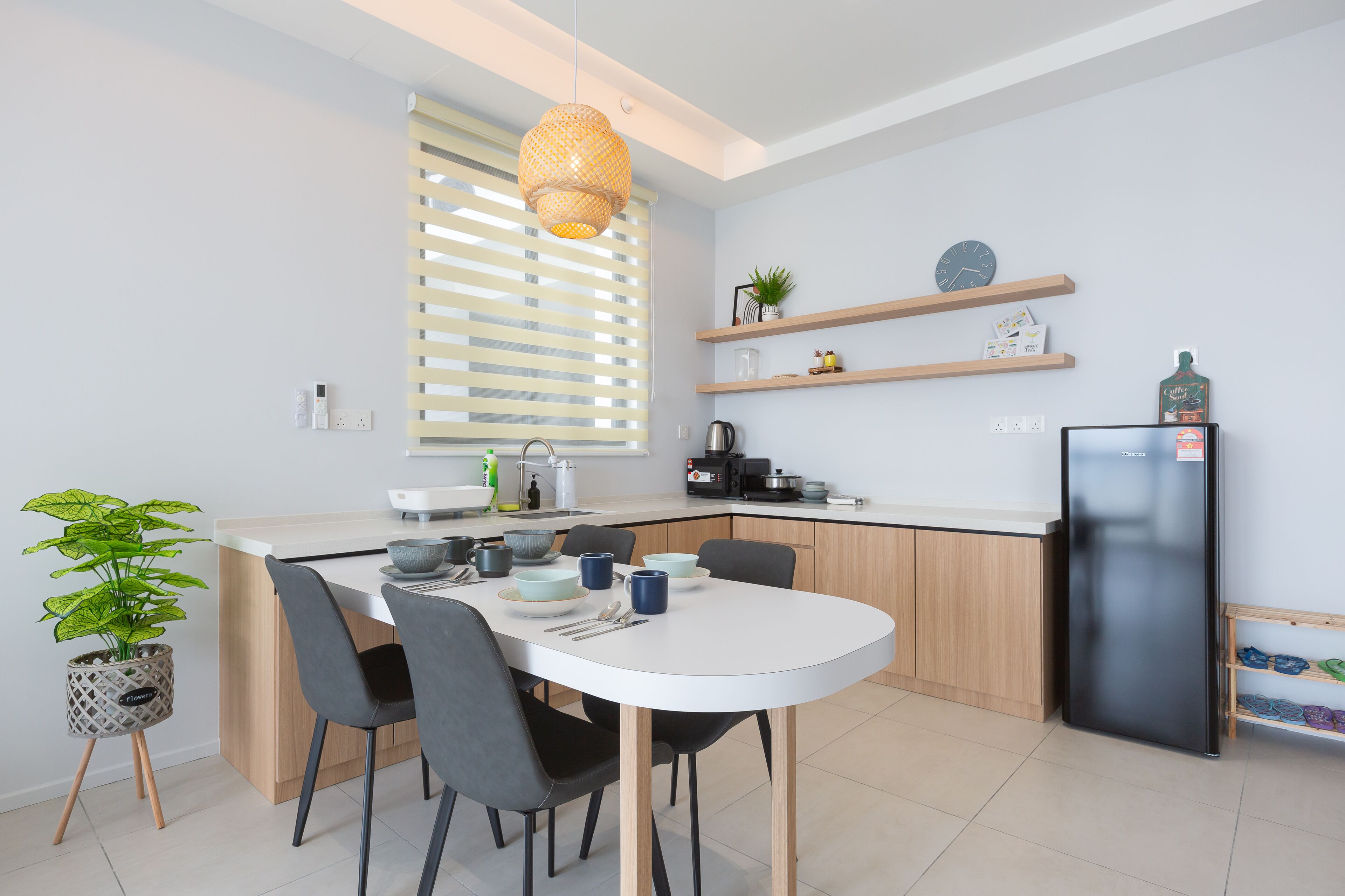 A modern kitchen with a white countertop, black chairs, a black refrigerator, and wooden shelves with kitchen items.