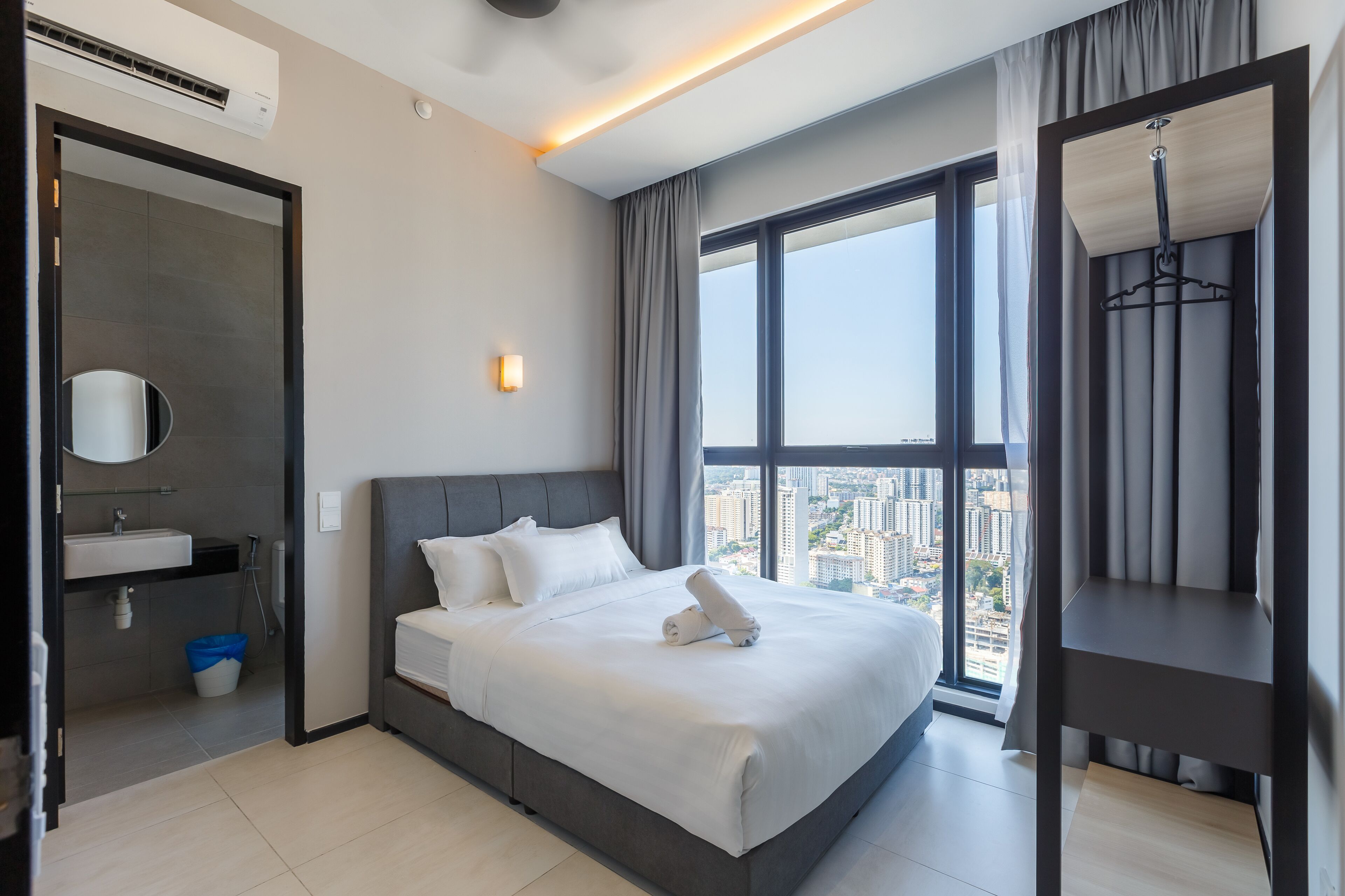 A modern hotel room with a large bed, a bathroom with a sink, and a city view through the window.