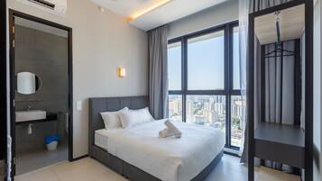 A modern hotel room with a large bed, a bathroom with a sink, and a city view through the window.