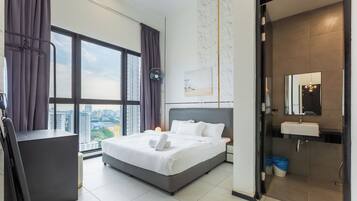 A modern hotel room with a large bed, a desk, a view of the city, and a bathroom with a sink and mirror.