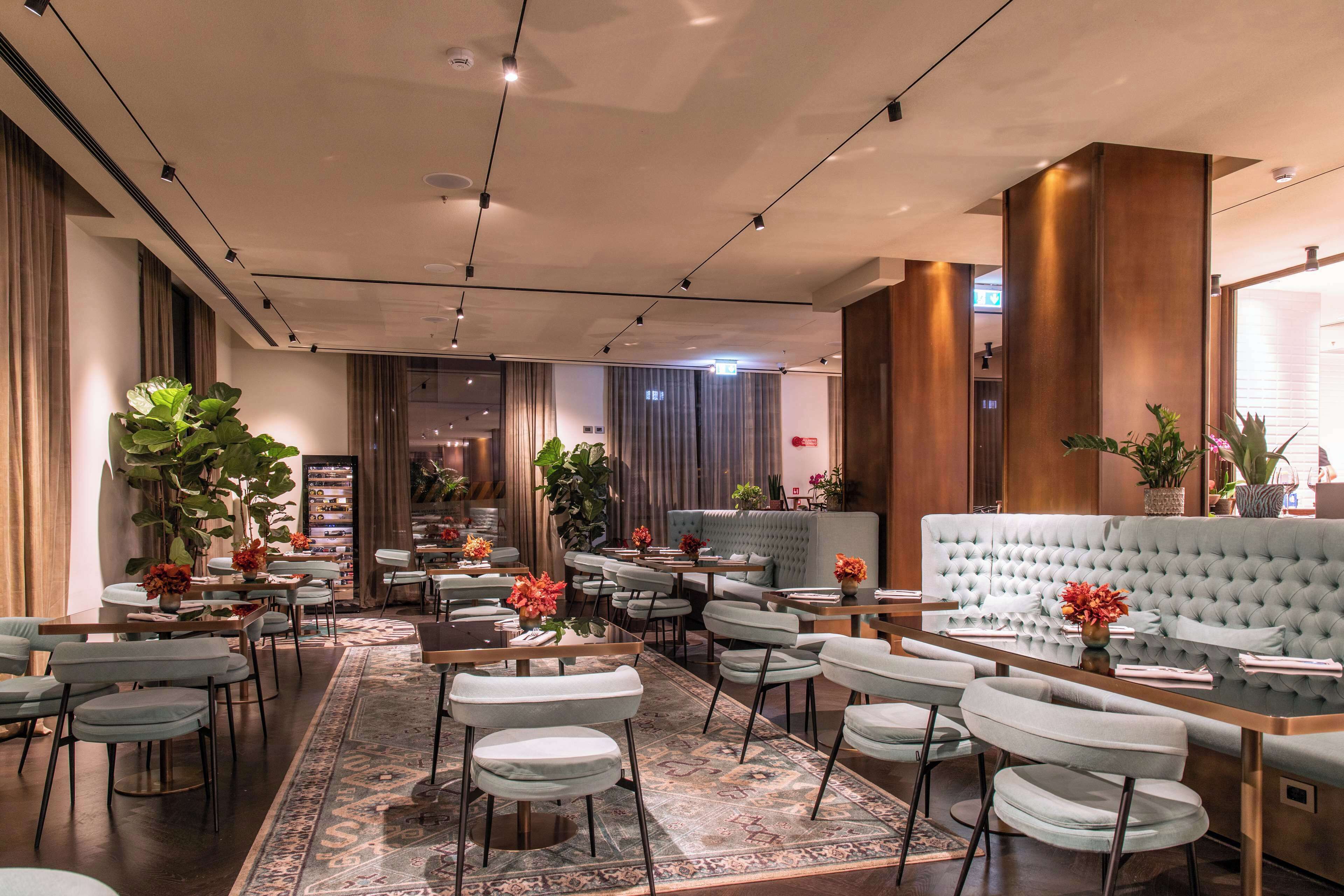 A modern hotel lobby with a central seating area, multiple tables, and a large sofa.