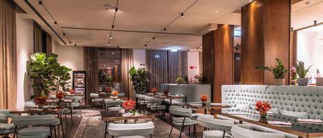 A modern hotel lobby with a central seating area, multiple tables, and a large sofa.