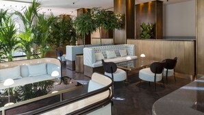 A modern lobby with a sofa, chairs, a coffee table, and potted plants. - Radisson Collection Hotel, Roma Antica (Rome)