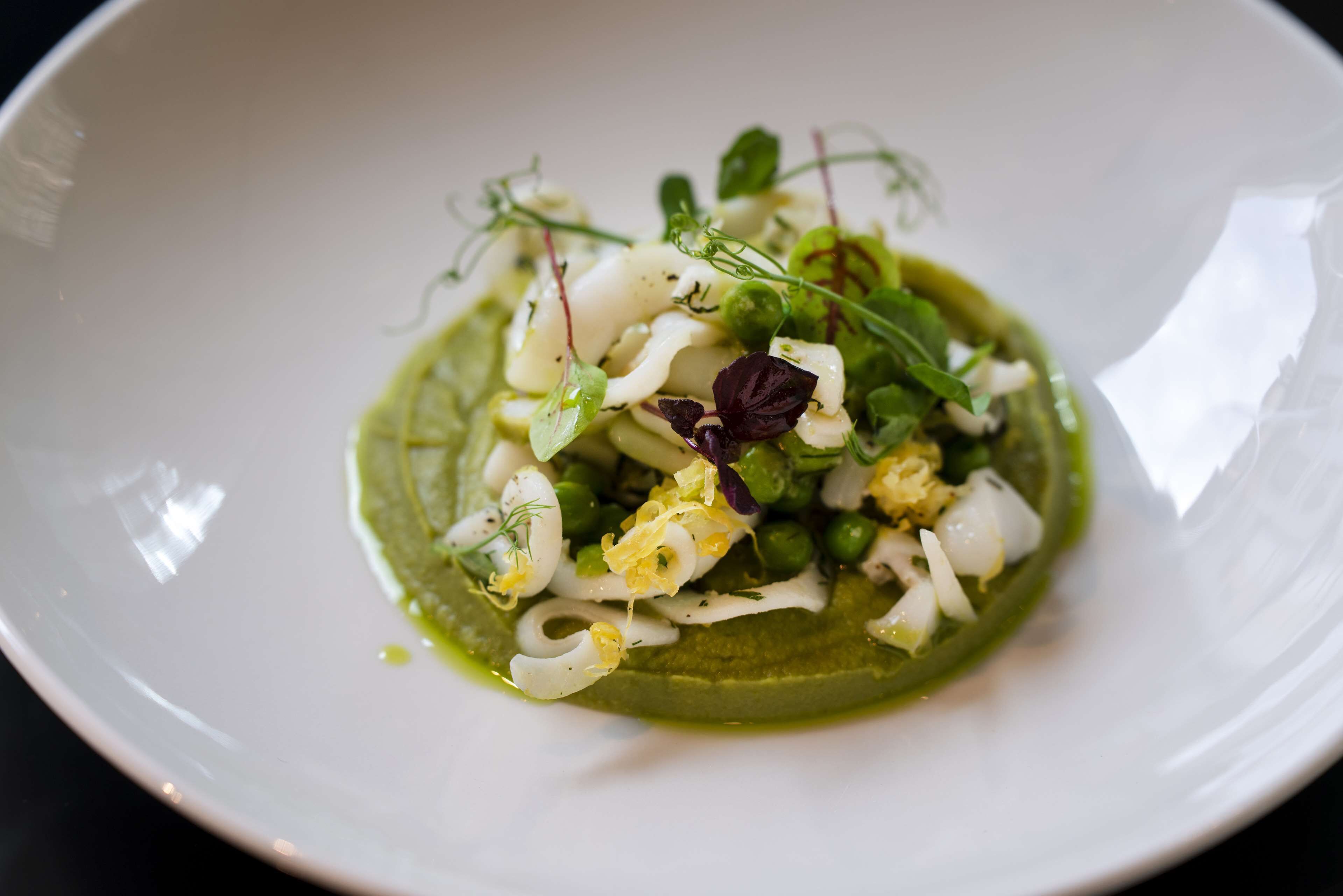 Un plato blanco con salsa verde, verduras blancas y verdes, y algunas hojas moradas.