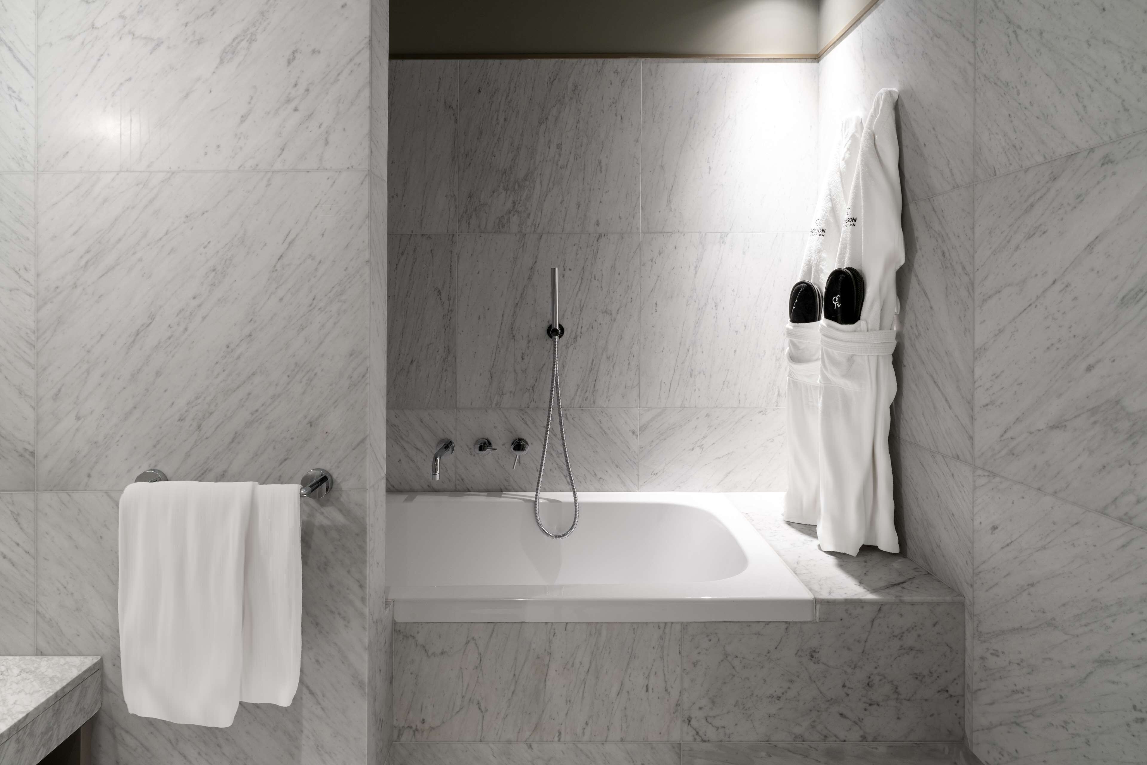 Une salle de bain moderne avec un sol et des murs en marbre, une baignoire, une douche et un porte-serviettes.