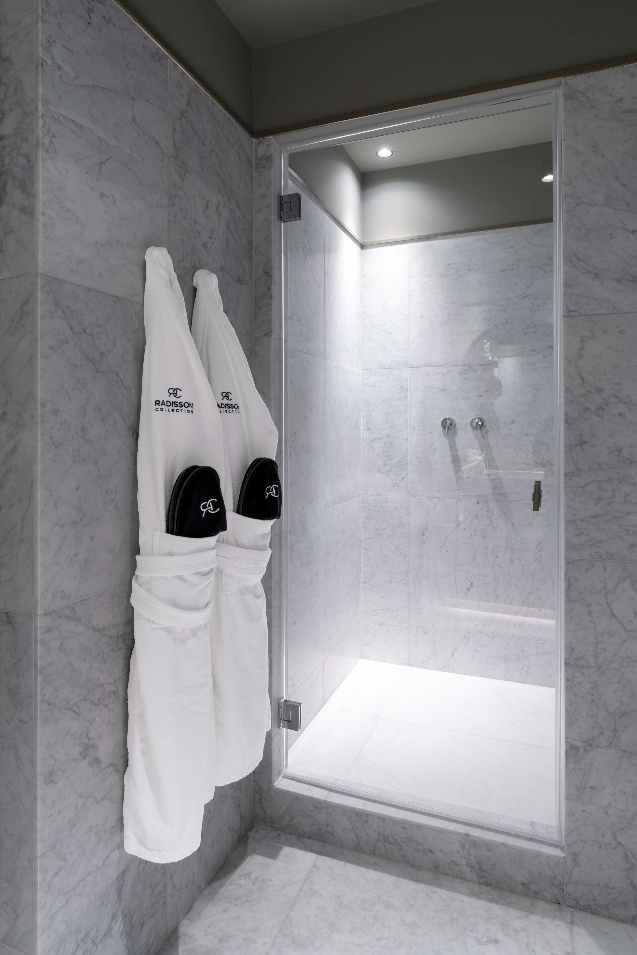 Ein modernes Badezimmer mit einer gläsernen Duschkabine, Marmorwänden und zwei weißen Handtüchern an einem Handtuchhalter.