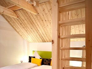 A bedroom with a sloped ceiling, a bed with pillows, and a window with a view. - The Rizzi - Detached vacation home with infinity pool in Southern Styria (Tillmitsch)
