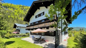 Un chalet de dos pisos con balcón, zona de estar al aire libre y vistas al bosque circundante.