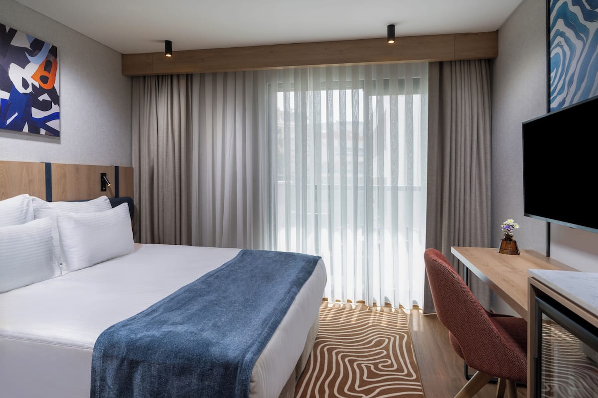 A hotel room with a large bed, a desk, a chair, and a TV.