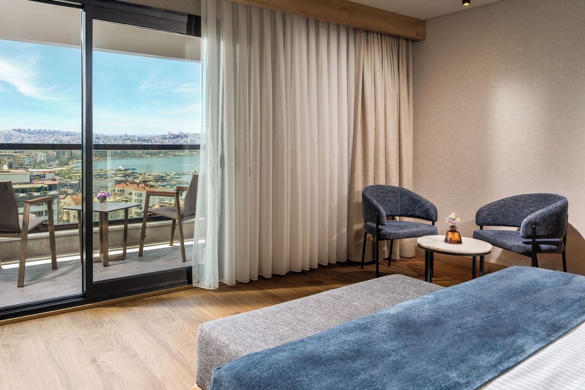 A modern hotel room with a balcony, two chairs, a small table, and a bed.