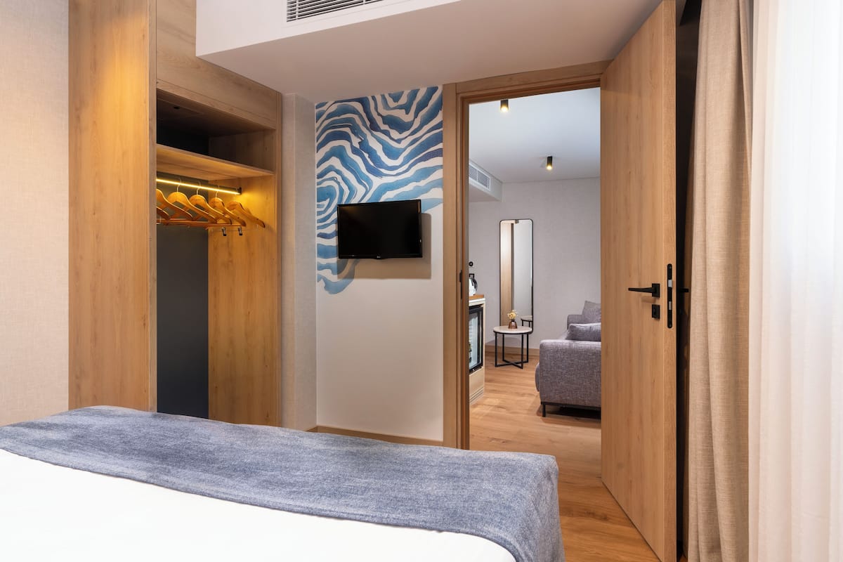 A modern hotel room with a bed, wooden wardrobe, a television mounted on the wall, and a mirror.