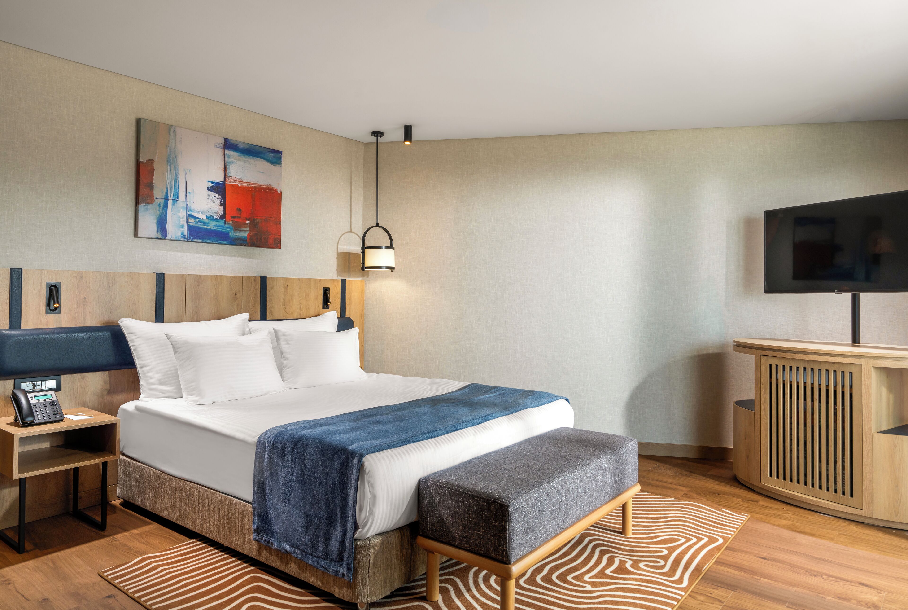 Una habitación de hotel moderna con una cama grande, una mesita de noche con teléfono, televisión y un armario de madera.