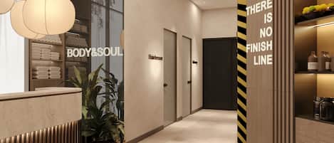 Un moderno vestíbulo de hotel con una recepción, una planta y una pared con un letrero que dice 'BODY&SOUL'.