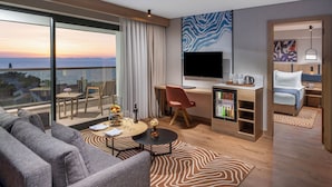 Una habitación de hotel moderna con un ventanal grande, un televisor de pantalla plana, un escritorio con una silla, un sofá y un minibar.