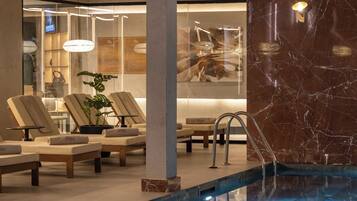 Zona de piscina con sillas de descanso, pared de mármol y un separador de vidrio.