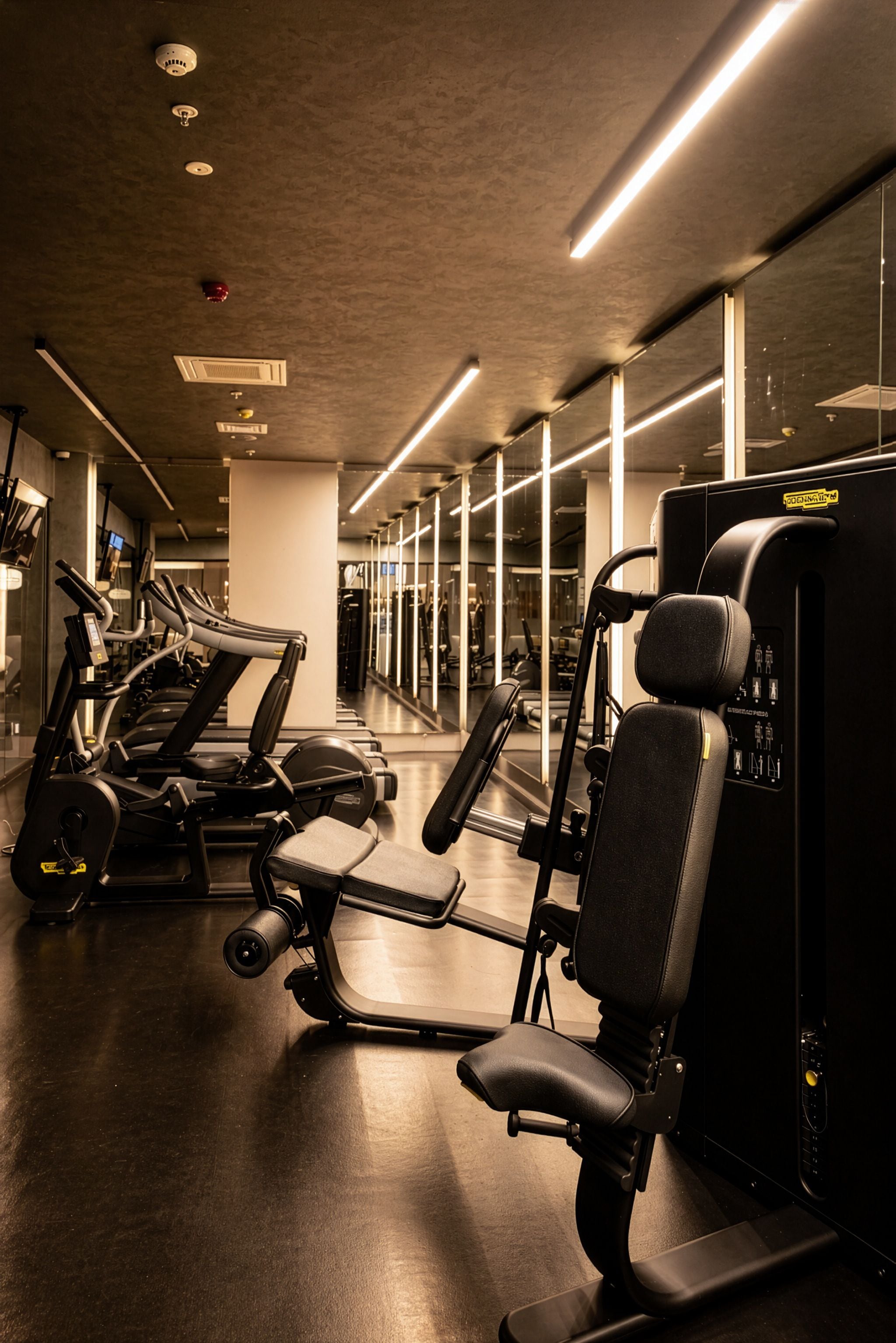 Un gimnasio con equipo de ejercicio, paredes espejadas y un diseño moderno.