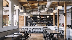 A restaurant with wooden tables and chairs, a bar area with shelves of bottles, and large windows allowing natural light. - Unique Modern Ranch with Pool, Hot Tub, Grill & Fireplace (Nashville)