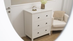 A white dresser with three drawers, a small clock, and a vase with flowers on top. - Stylish apartment 2 min from the Dragon Bridge (Ljubljana)