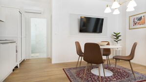 A modern kitchen with white cabinets, a dining area with a round table, brown chairs, and a red and blue patterned rug. - Stylish apartment 2 min from the Dragon Bridge (Ljubljana)