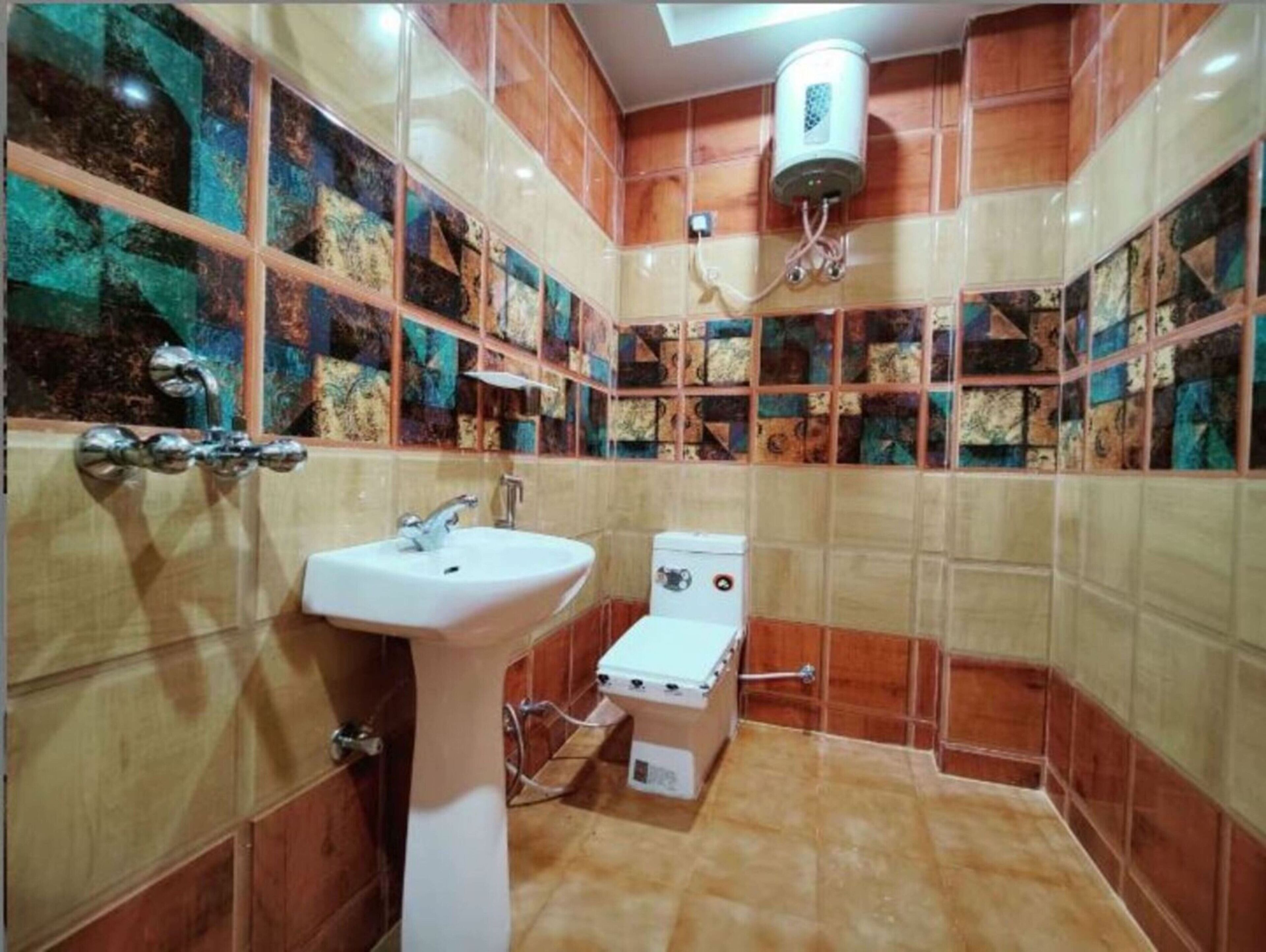 A bathroom with a sink, toilet, and shower. The walls are tiled with a mosaic pattern.