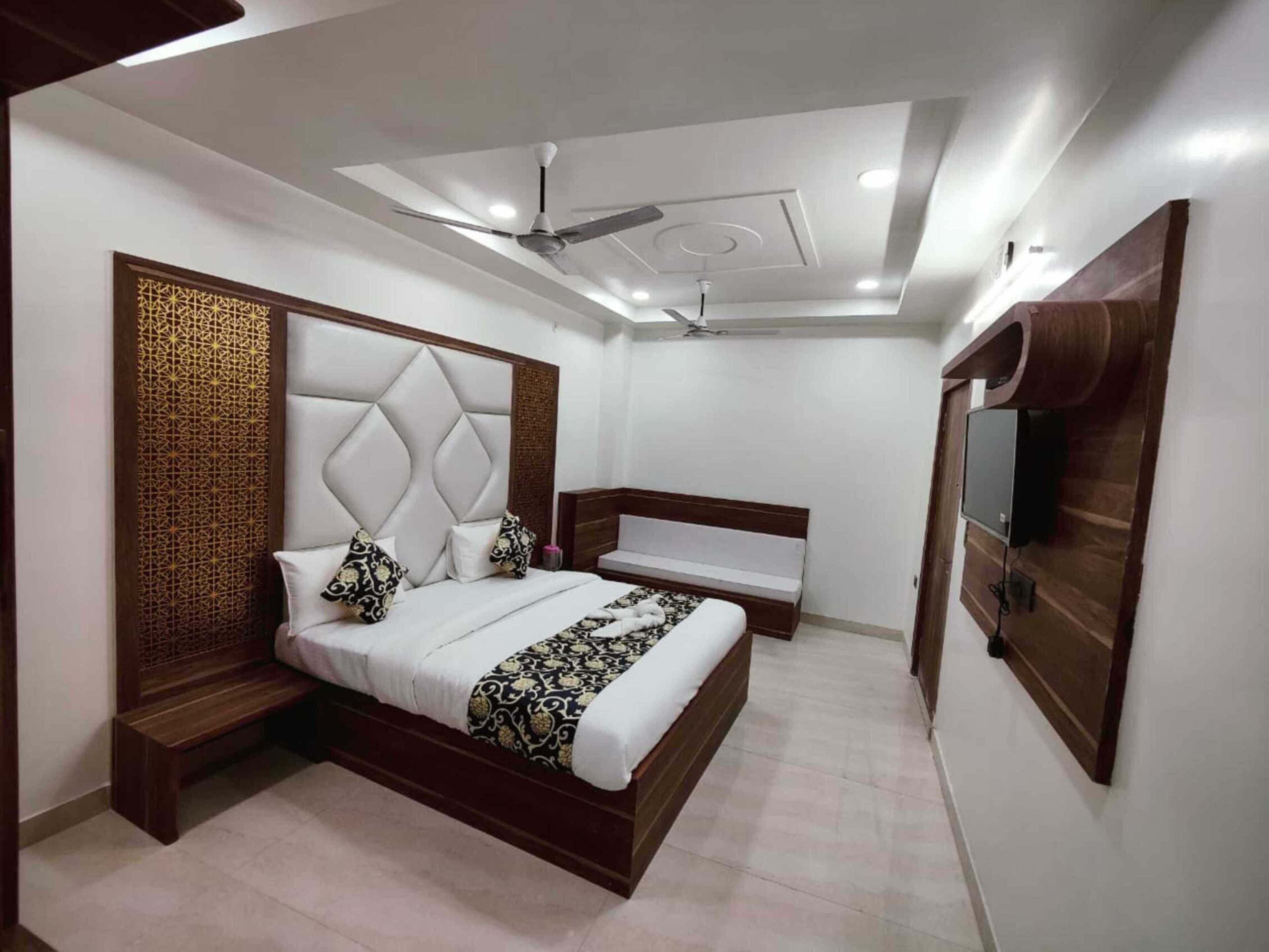 A modern bedroom with a bed, a bench, a TV, and a ceiling fan.