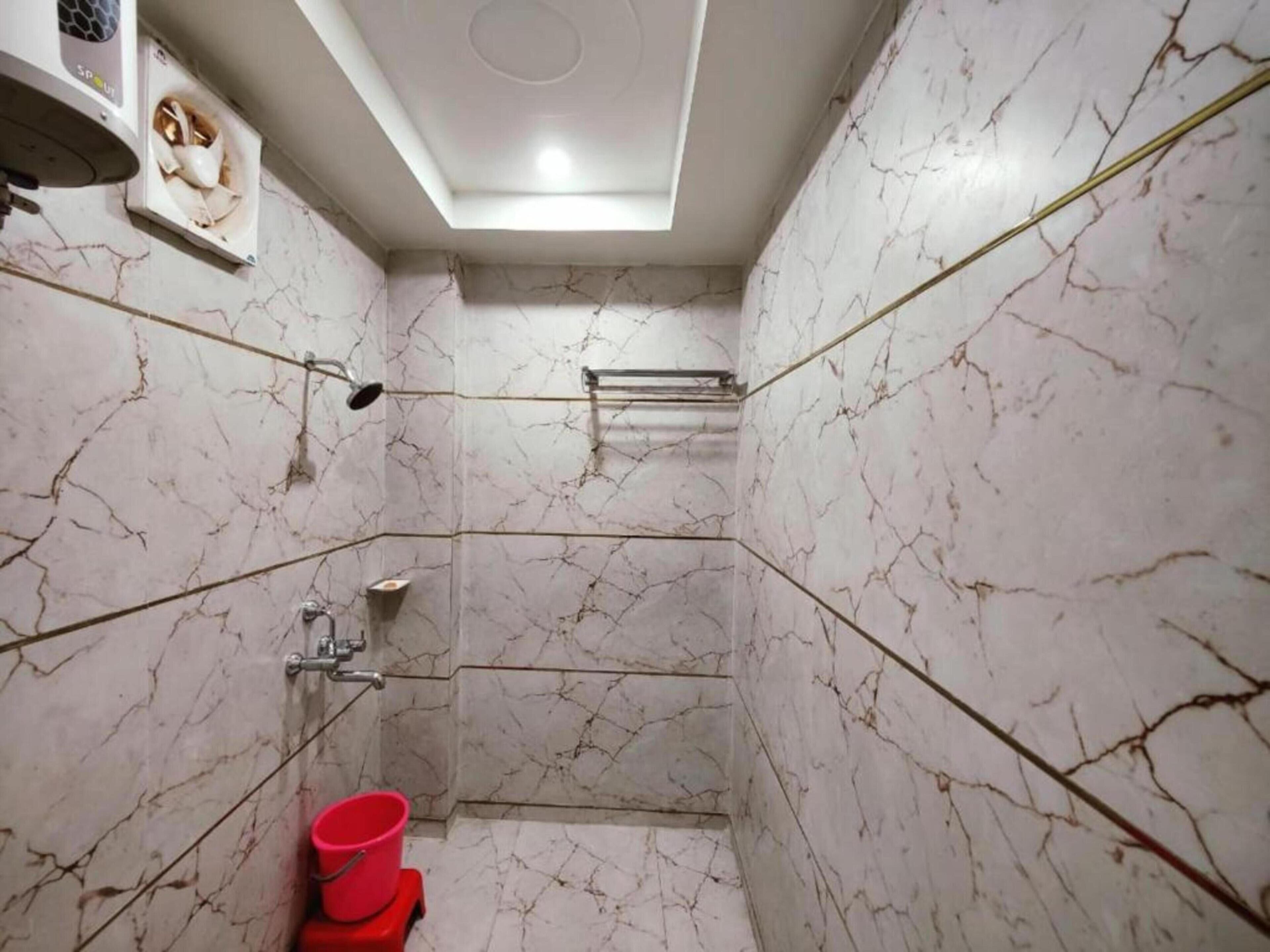 A bathroom with marble walls, a shower, a red bucket, and a ceiling light.